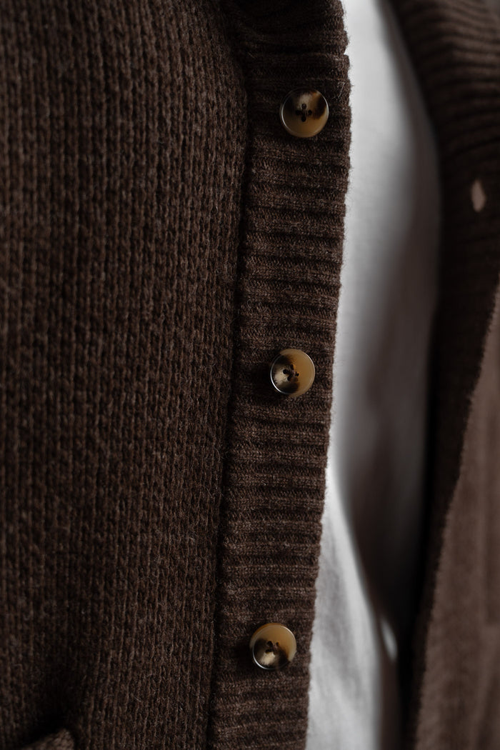 Close-up of a brown knit cardigan with four buttons over a white shirt, highlighting texture and detail.