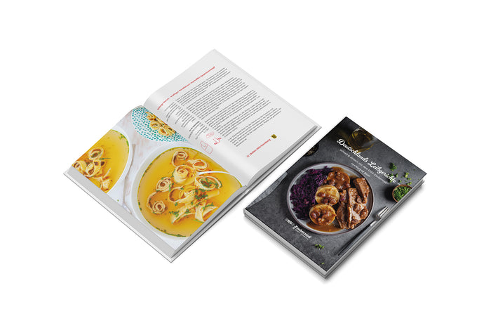 Auf einer weiรen Flรคche sind zwei Kochbรผcher โESGE-Zauberstab Deutschlands-Leibgerichteโ abgebildet โ eines geschlossen mit einem Gericht aus Fleisch, Kartoffeln und Rotkohl, das andere aufgeschlagen mit einem Suppenrezept mit Nudeln und Krรคutern.