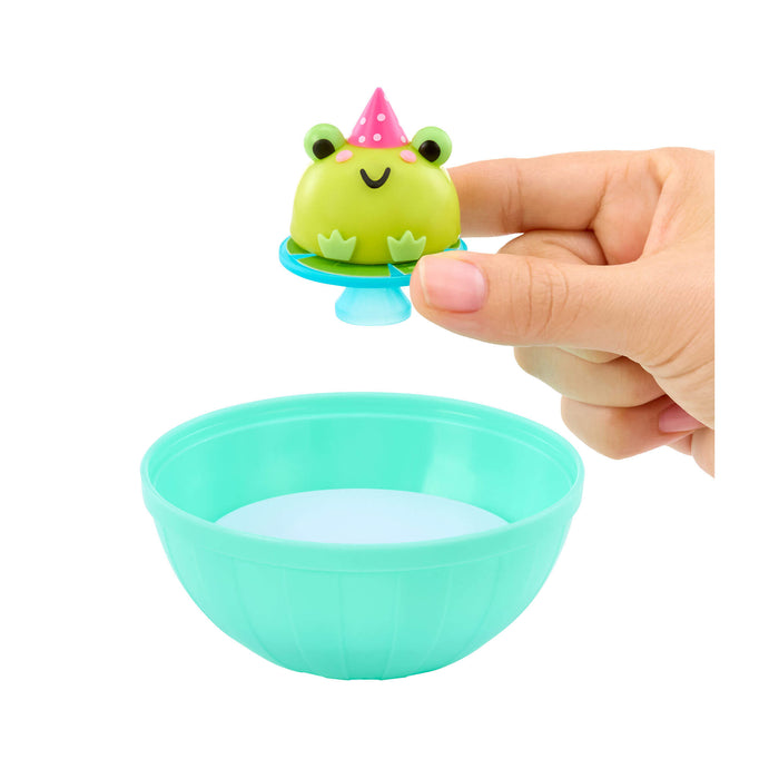 Small green frog toy with a pink party hat on top of a teal bowl held by a hand.