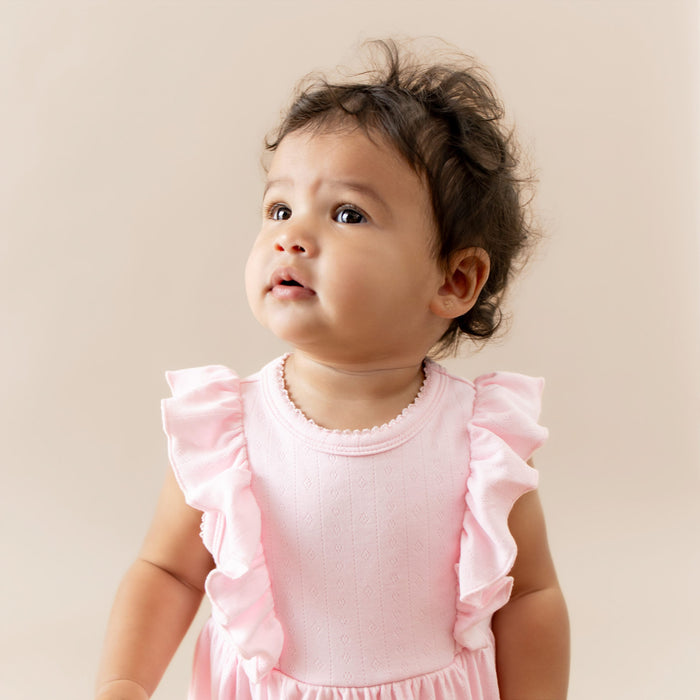 Baby wearing a pink dress with ruffled sleeves against a beige background