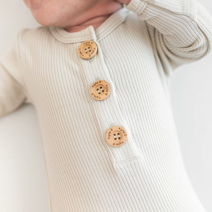 Close-up of a beige ribbed gown with wooden buttons on a white background