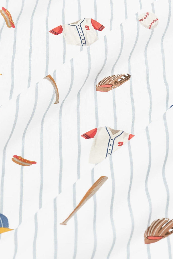 Close up of bamboo fabric: An all-over print featuring baseballs, wooden baseball bats, catcherβs mitts, white baseball jerseys with red sleeves and a red number 9, blue baseball caps with a yellow brim, and a hot dog, over a white background with dusty blue pinstripes.