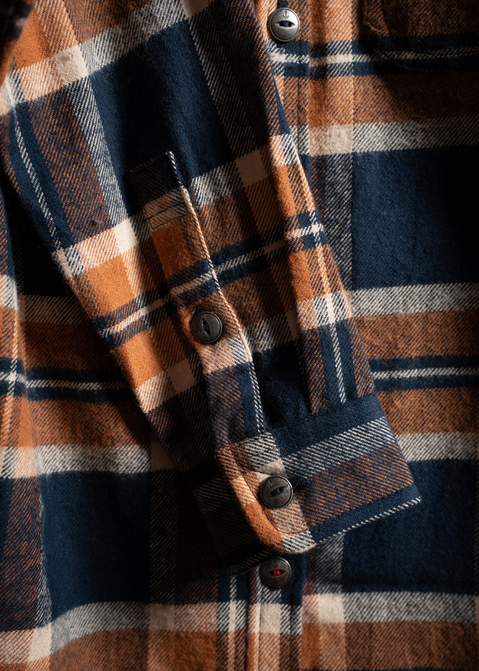Close-up of a plaid shirt with orange, navy, and white checks, featuring black buttons and a folded cuff.