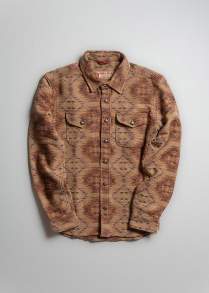 Patterned button-up shirt with earthy tones, featuring geometric designs. Long sleeves and dual chest pockets on a plain background.