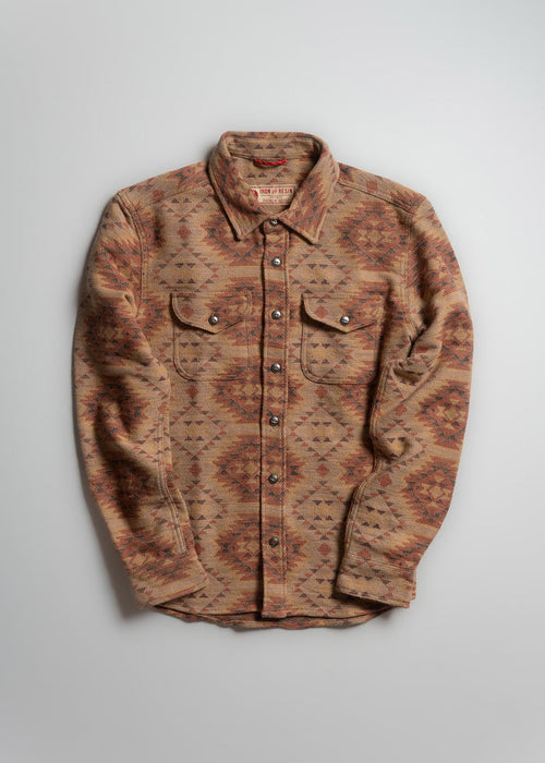 Patterned button-up shirt with earthy tones, featuring geometric designs. Long sleeves and dual chest pockets on a plain background.