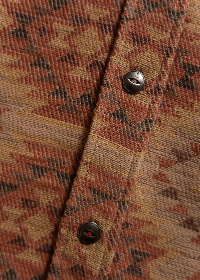 Close-up of a textured fabric with a geometric pattern in earthy tones, featuring metal buttons along a central seam.