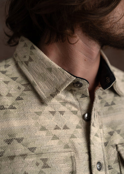 Close-up of a man wearing a patterned beige shirt with triangle designs, highlighting the collar and button details.