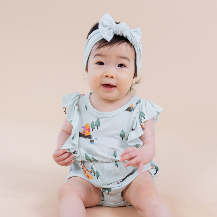 Close up of an infant wearing the Bubble Romper in Winnie the Pooh Hundred Acre Wood sitting on the floor