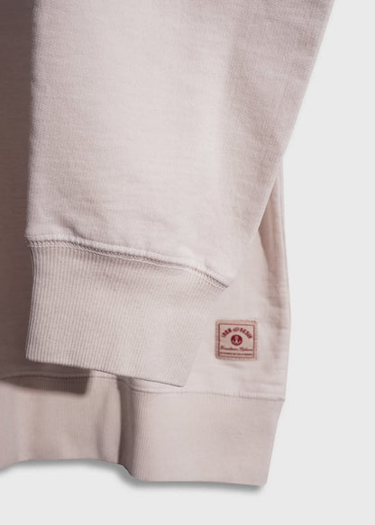 Close-up of a beige sweatshirt sleeve with ribbed cuff and a small red label near the hem on a light background.