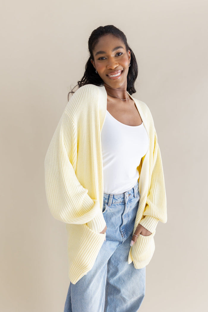 Female model posing wearing the Chunky Knit Women's Oversized Cardigan in Chamomile overtop a white tank top and light wash jeans