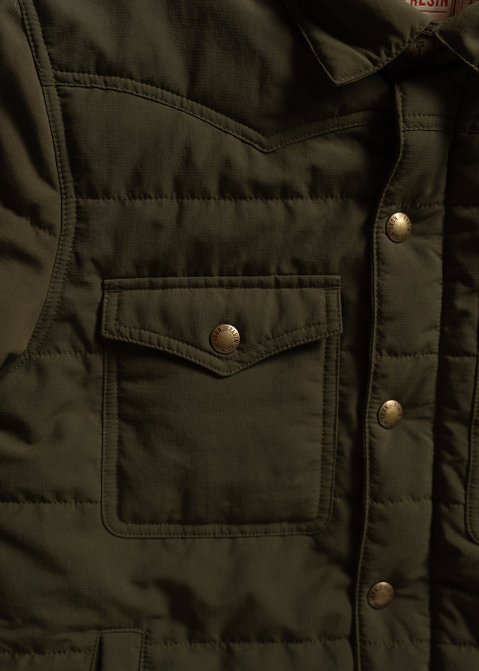 Close-up of an olive green quilted jacket with a front pocket and metallic snap buttons, highlighting its rugged texture.