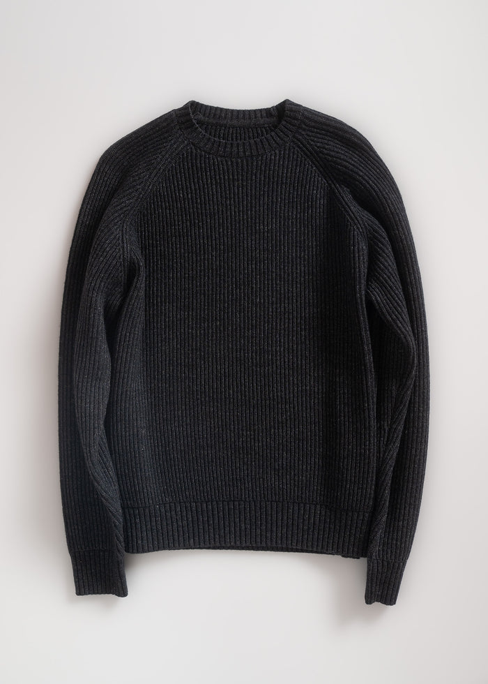 A black ribbed sweater with long sleeves and a round neck, neatly laid flat on a light surface, showcasing its texture and design.