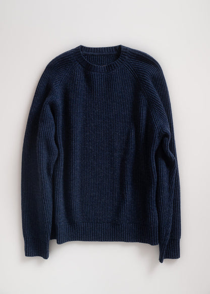 A navy blue ribbed sweater is laid flat on a light background, showcasing its texture and classic crew neck design.