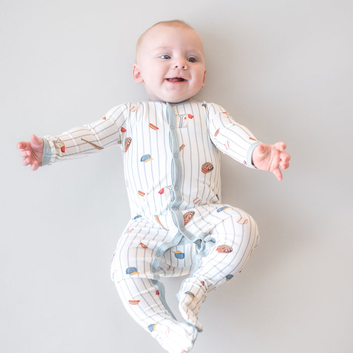 Smiling infant laying on a light surface wearing the Footie in Home Run
