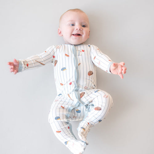 Smiling infant laying on a light surface wearing the Footie in Home Run