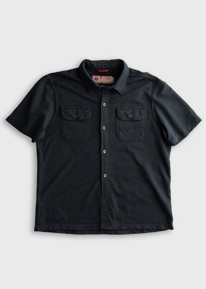 Dark short-sleeve button-up shirt with two chest pockets and a collar, displayed on a plain background.