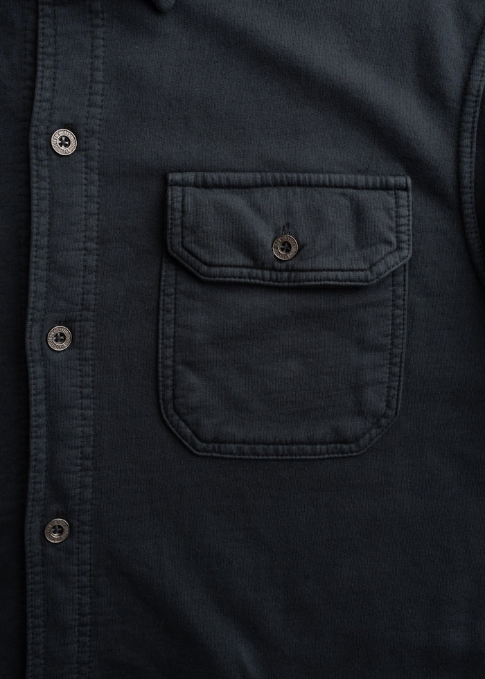 Close-up of a dark shirt with a buttoned pocket and row of buttons, highlighting its texture and design details.