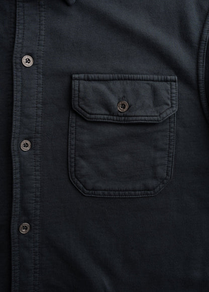 Close-up of a dark shirt with a buttoned pocket and row of buttons, highlighting its texture and design details.