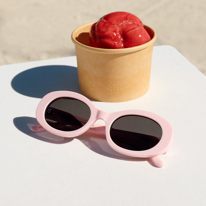 still life - diff eyewear lainey oval sunglasses with a powder pink frame and grey polarized lenses laying on a table next to ice cream