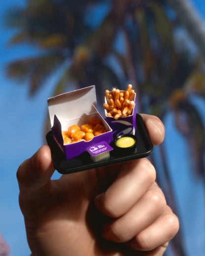 Hand holding a small black tray with Miniverse chicken nuggets and nacho cheese fries containers against a blurred background.
