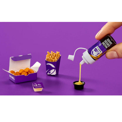 Hand pouring sauce from a bottle into a small container next to Taco Bell food items on a purple background