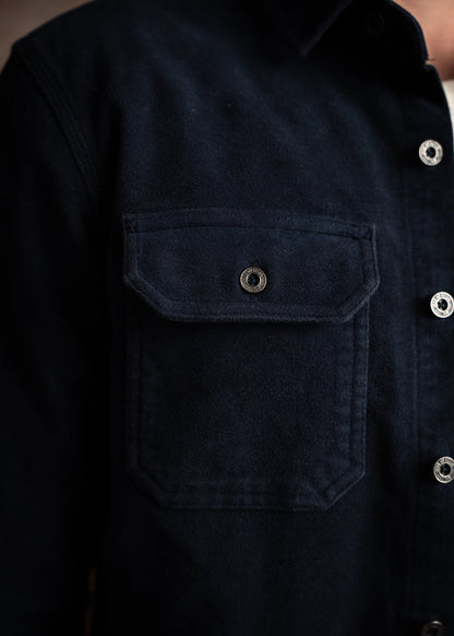Close-up of a navy blue shirt with a buttoned flap pocket, highlighting its texture and details against a soft background.