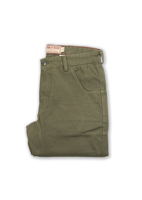 Olive green pants folded neatly, featuring a button closure and side pocket. Visible "Iron & Resin" label on the waistband.
