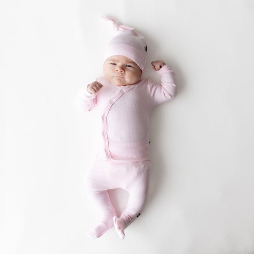 Newborn laying on a white surface wearing the Pointelle Take Me Home Set with Cap in Sakura with the picot trim visible