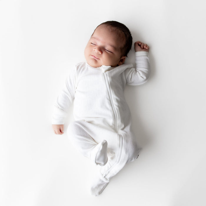 Sleeping newborn posing wearing the Pointelle Zippered Footie in Cloud