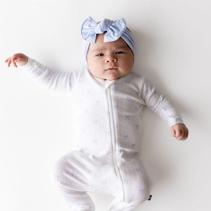 Close up of newborn wearing the Pointelle Zippered Footie in Sweet Blue Bow with a matching light blue bow
