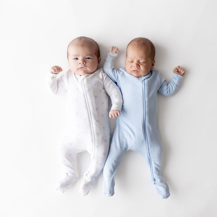 Two newborn laying side by side wearing the Pointelle Zippered Footie in Sweet Blue Bow and Breeze