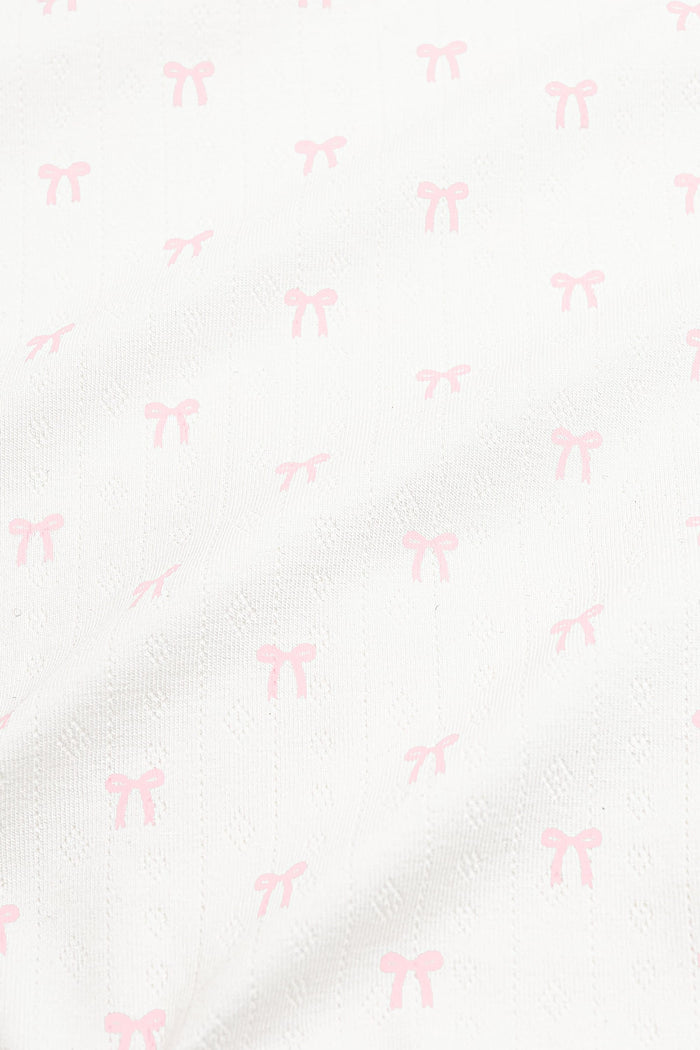 Close up of the pointelle fabric: An all-over print of dainty light pink bows over a white background.
