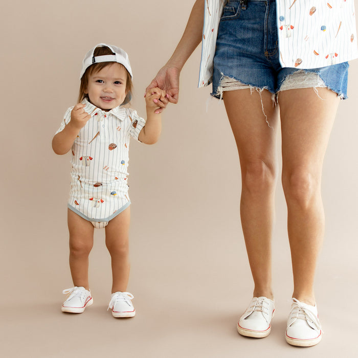 Young toddler wearing the Polo Bodysuit Home Run standing beside his mother holding her hand