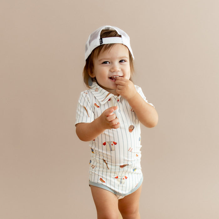 Close up of young boy wearing the Polo Bodysuit Home Run with a backwards baseball cap