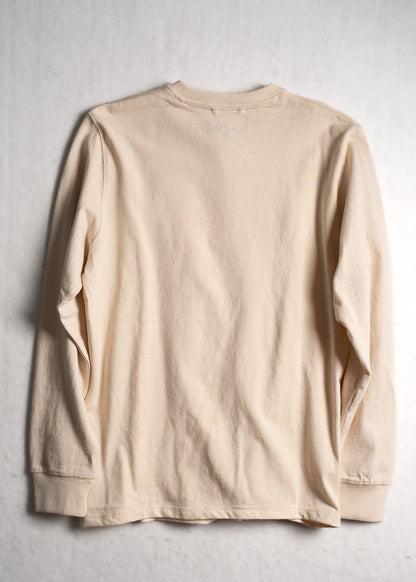 A beige long-sleeve shirt is laid flat on a light background, showcasing its simple design and ribbed cuffs.