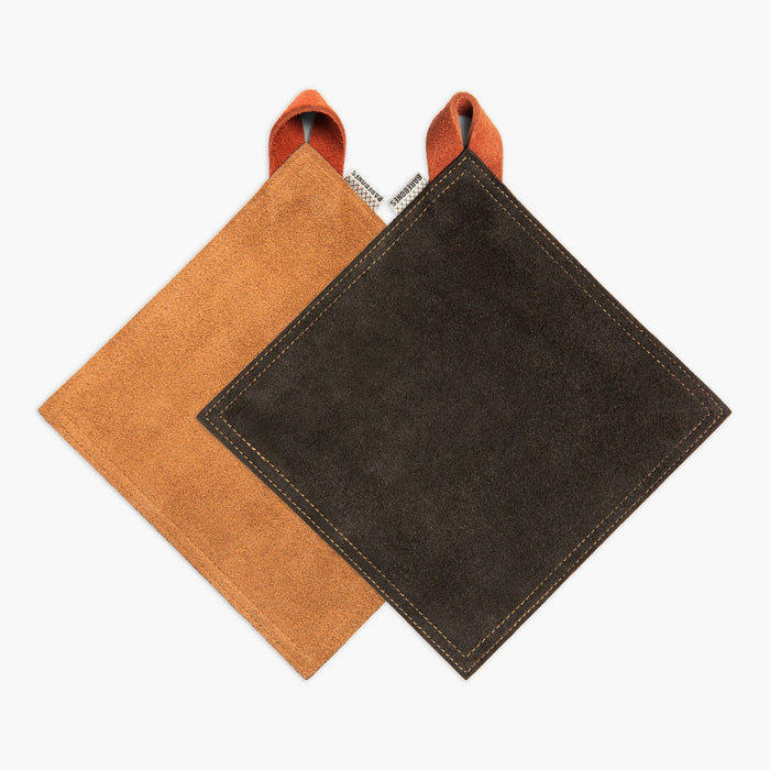 Two suede pot holders, one Tan and one Black, both with a Terracotta hanging strap, on a white background.