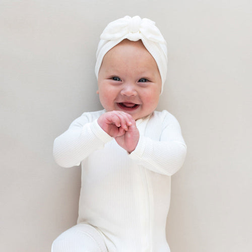Smiling infant wearing Kyte Baby Ribbed bamboo Headwrap in Cloud and Ribbed Zippered Romper in Cloud
