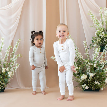 Two children wearing Kyte Baby Ribbed Henley Sets in Cloud and Oat