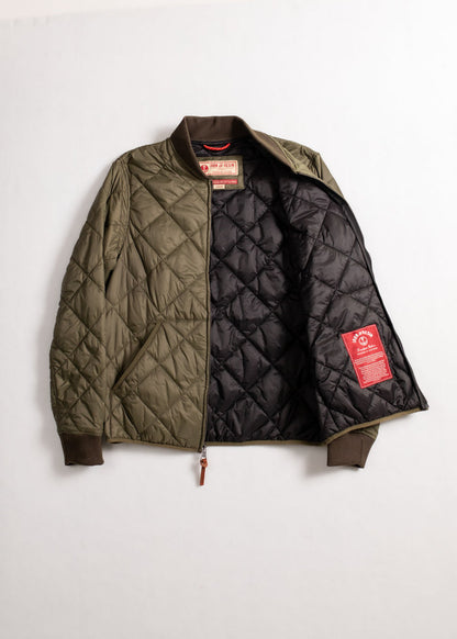 Olive quilted jacket with brown cuffs, open to show black lining and red label. Simple, stylish outerwear on a plain background.