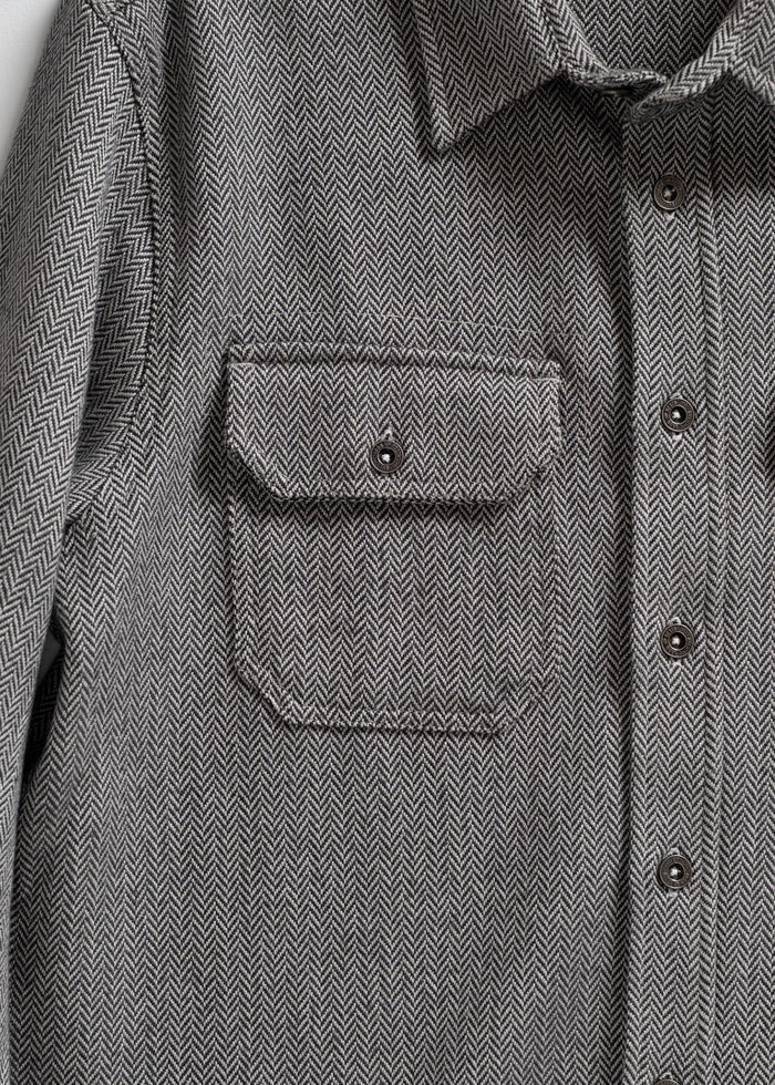 Gray herringbone shirt with buttoned front and chest pocket, showcasing detailed fabric pattern and classic design.
