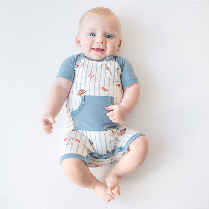 Young boy wearing the Shortall in Home Run laying on a light cream surface