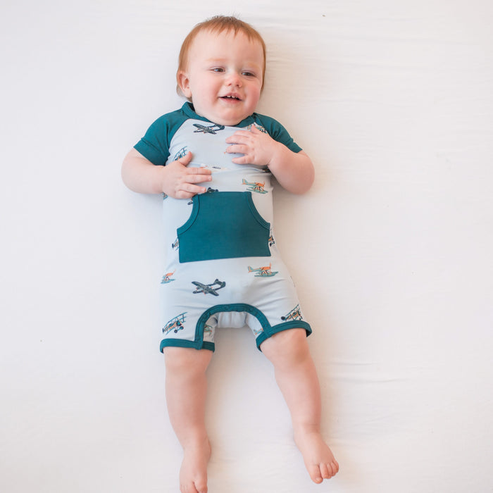 Toddler laying on a white surface wearing the Shortall in Take Off with a Loch colored trim