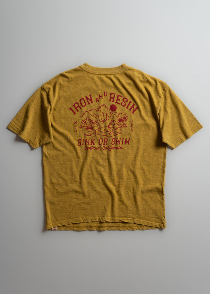 Yellow T-shirt with "Iron and Resin" and "Sink or Swim" in red text, featuring a hand and wave graphic. Ventura, California.