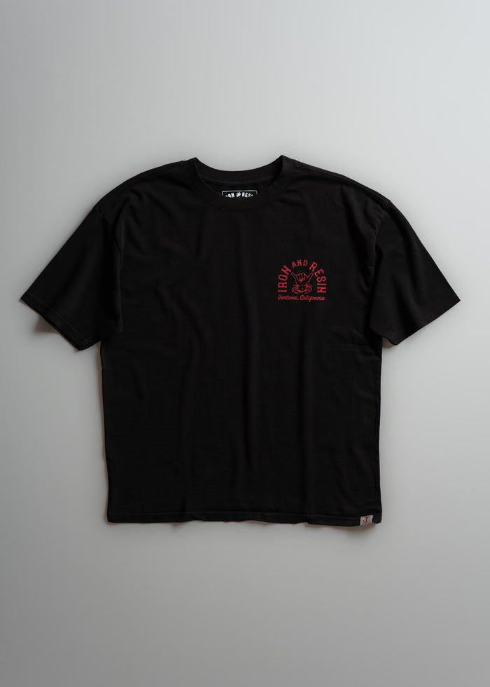 Black T-shirt with "Iron and Resin, Ventura, California" in red on chest. Casual style, short sleeves, laid flat on gray background.