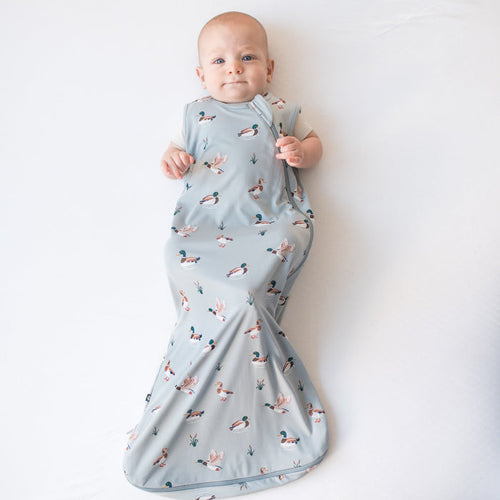 Infant laying on a white surface wearing the Sleep Bag in Mallard