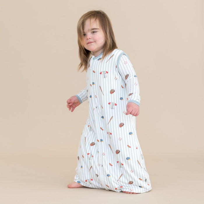 Young child walking wearing the Sleep Bag Walker in Home Run 0.5 with matching long sleeve pajamas on underneath