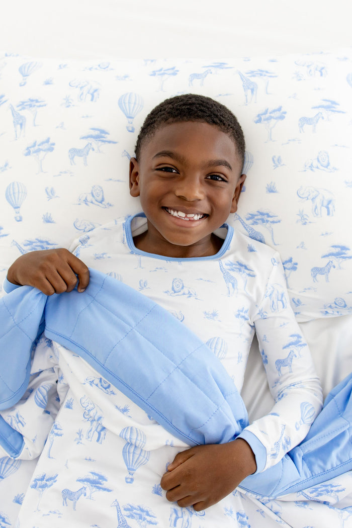 Young smiling boy laying on a Standard Pillowcase in Toile Safari with the matching blanket over top of him