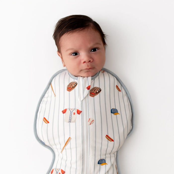 Close up of newborn wearing the Swaddle Bag in Home Run 0.5 laying on a white surface