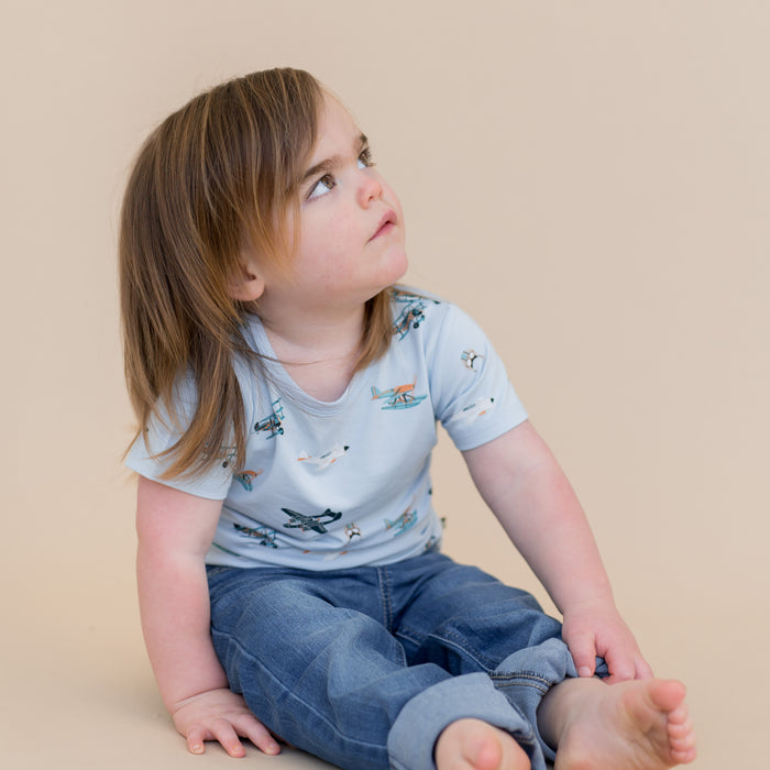 Young child sitting on the floor wearing the Toddler Basic Tee in Take Off paired with medium wash jeans