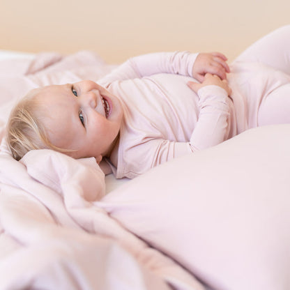 Toddler girl laying on a toddler bed with a blush pink blanket and pillow